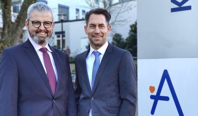 Zwei Männer in Anzügen stehen vor einem Eingangsschild mit dem Augustinus Logo.