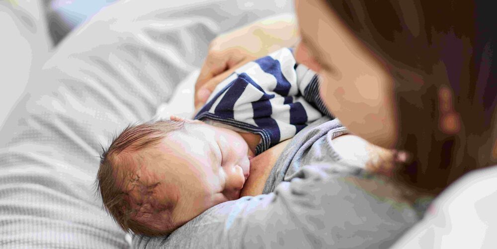 Eine Mutter stillt ihr Baby. Der Blick auf das Baby fällt über die Schulter der Mutter.